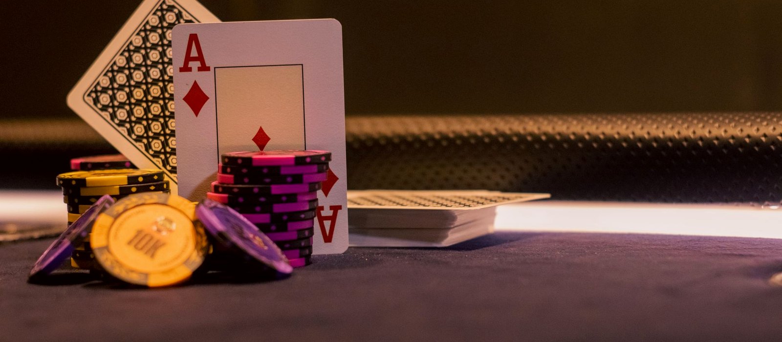 Low-key still life of a roulette wheel at rest, a fanned deck of cards, dice and unmarked chips on dark felt