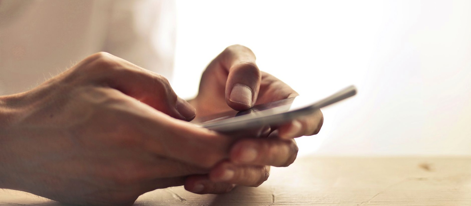 An adult hand placing a smartphone face down on a timber table and letting go